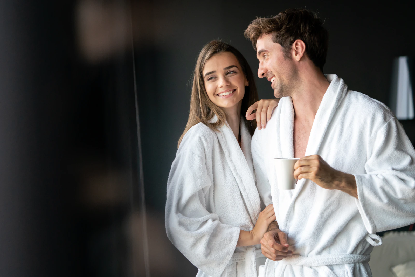 Hotelgäste im Spa-Bademantel: Ein Paar lacht sich zu, der Mann hält eine Tasse Kaffee.